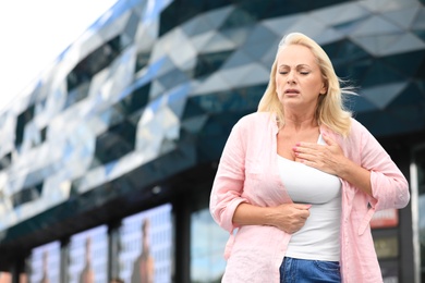 Mature woman suffering from heart attack outdoors. Space for text