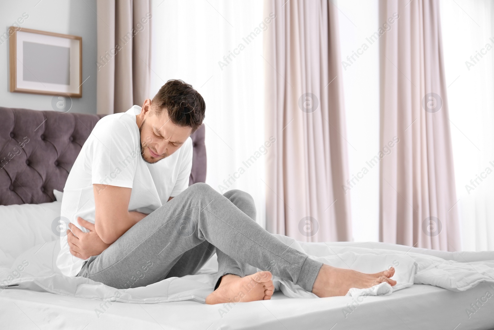 Photo of Man suffering from abdominal pain in bedroom