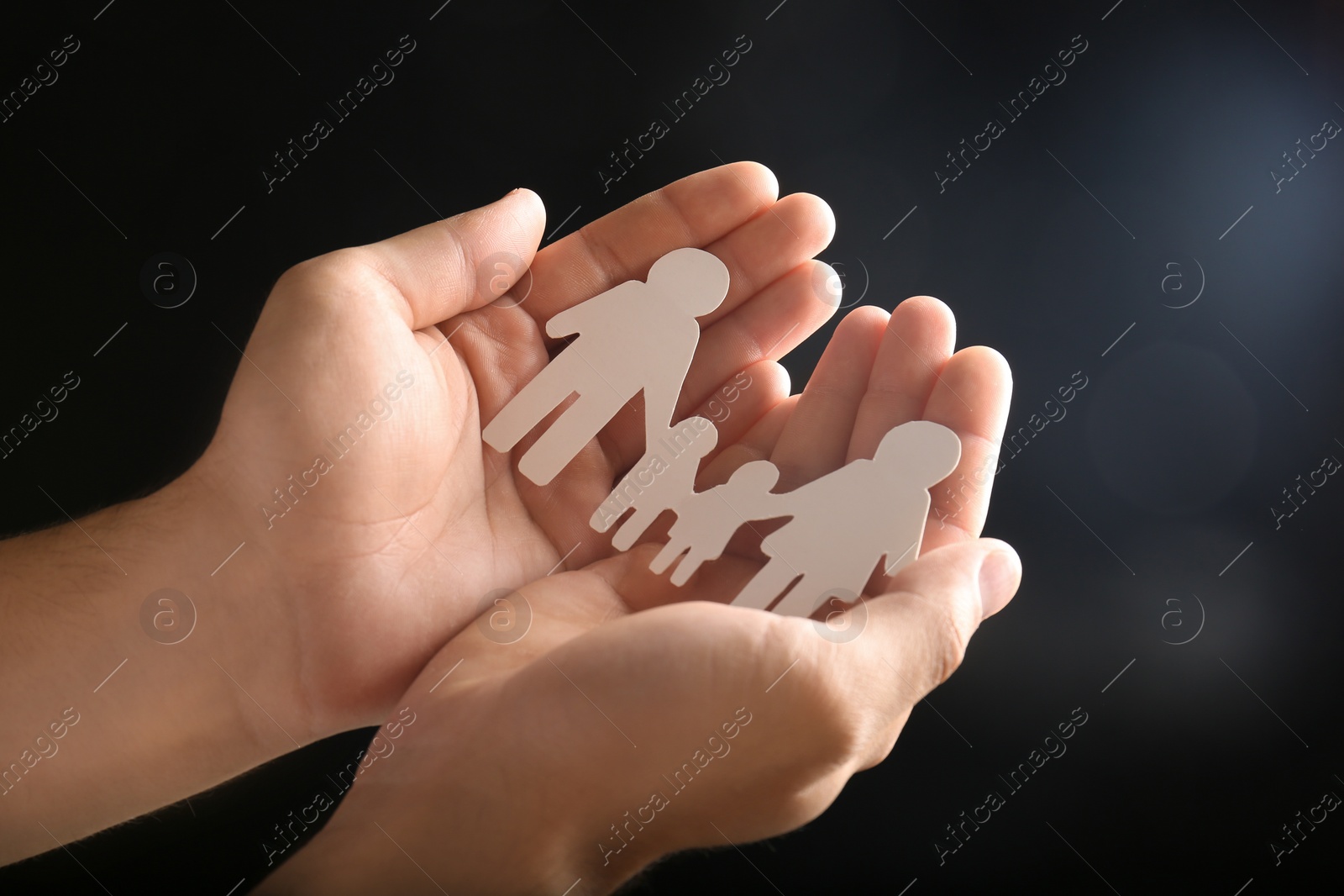 Photo of Man holding paper silhouette of family in hands on dark background, closeup