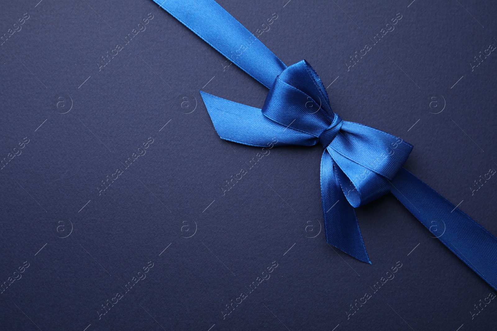 Photo of Bright satin ribbon with bow on blue background, top view. Space for text