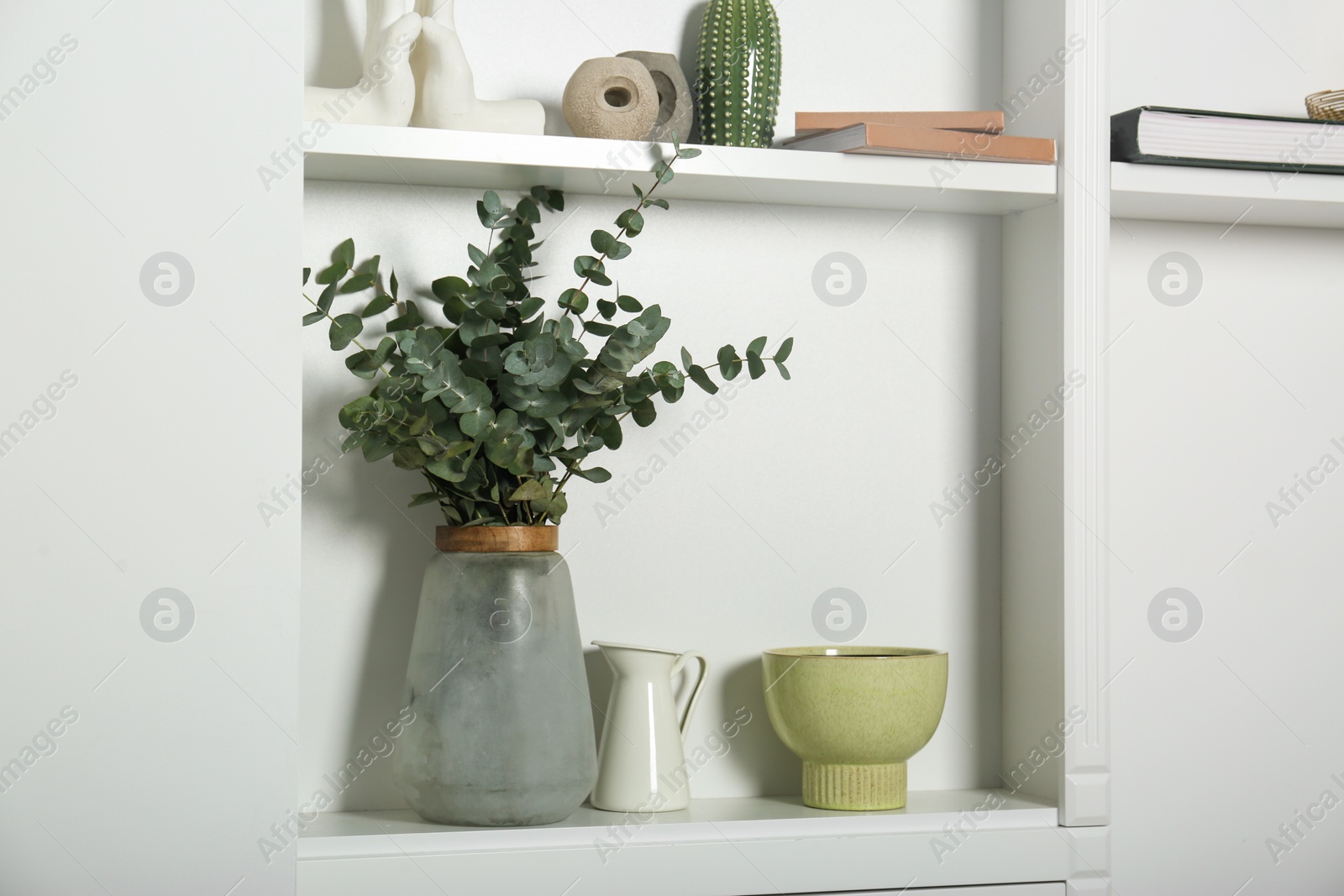 Photo of White shelves with books, eucalyptus and different decor indoors. Interior design