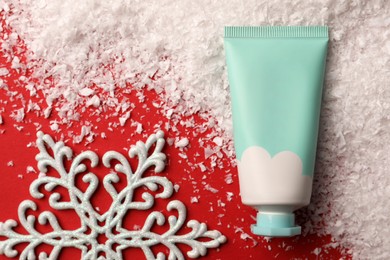 Photo of Winter skin care. Hand cream and artificial snow on red background, flat lay