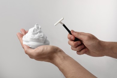 Man holding shaving foam and razor on light grey background, closeup