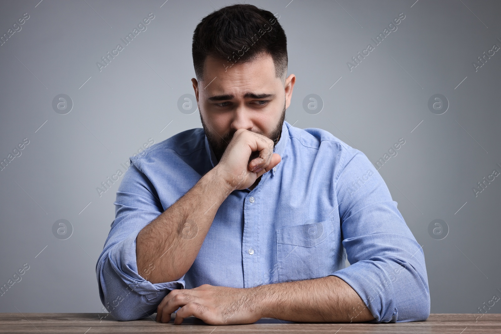 Photo of Portrait of sad man at wooden table on light grey background