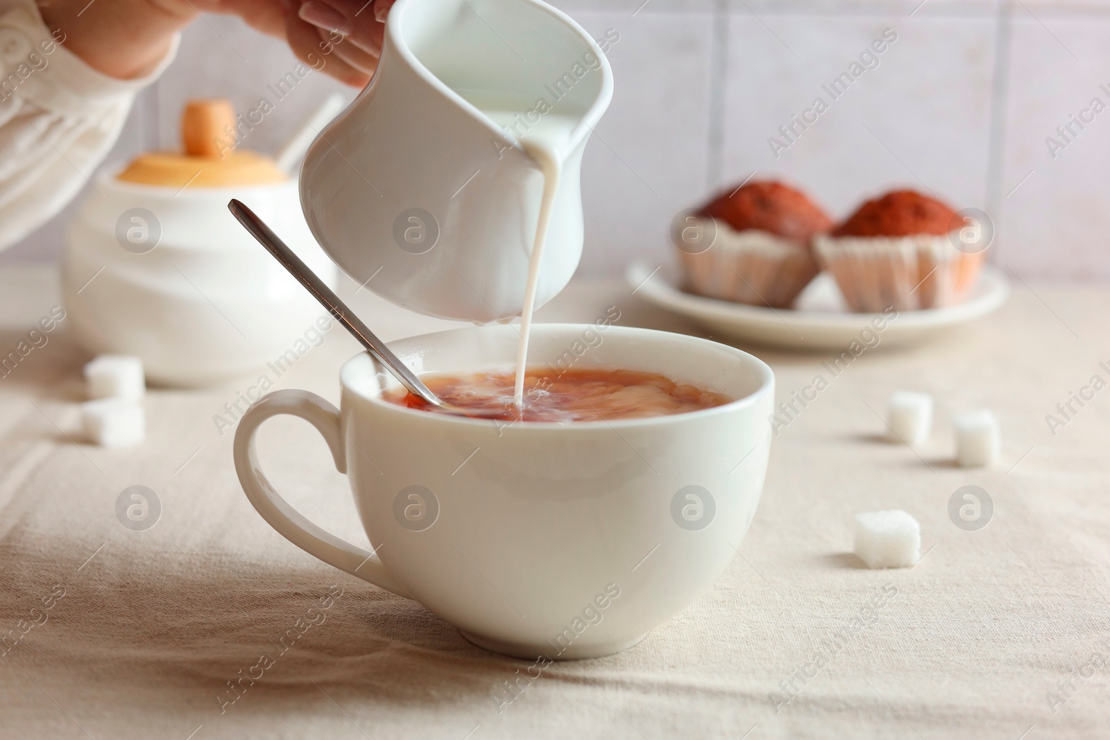 Photo of Pouring milk into cup with tea on light table, closeup