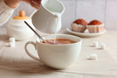 Pouring milk into cup with tea on light table, closeup