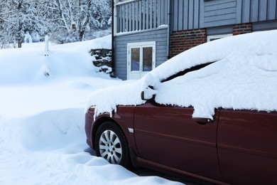 Modern car covered with snow near building on winter day