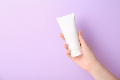 Photo of Woman with tube of cream on lilac background, closeup