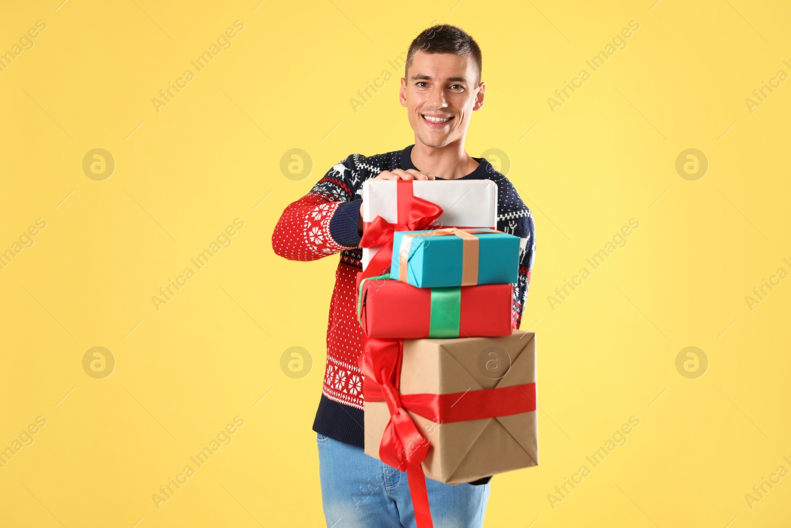 Photo of Happy man in Christmas sweater holding gift boxes on yellow background