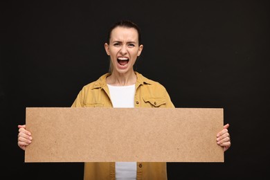 Screaming woman holding blank cardboard banner on black background, space for text