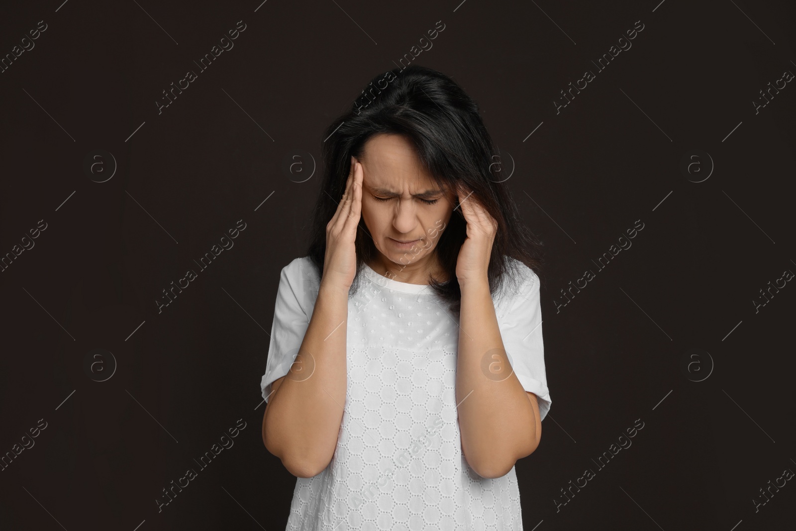 Photo of Mature woman suffering from headache on dark brown background