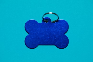 Photo of Pet tag in shape of bone with ring on light blue background, top view