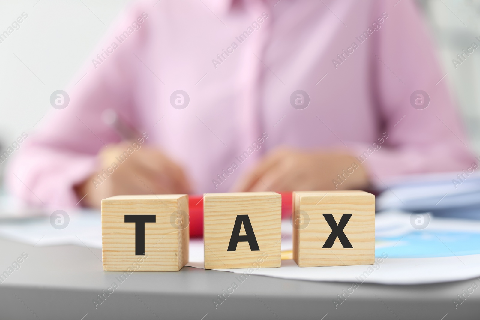 Photo of Wooden cubes with word TAX and blurred woman on background