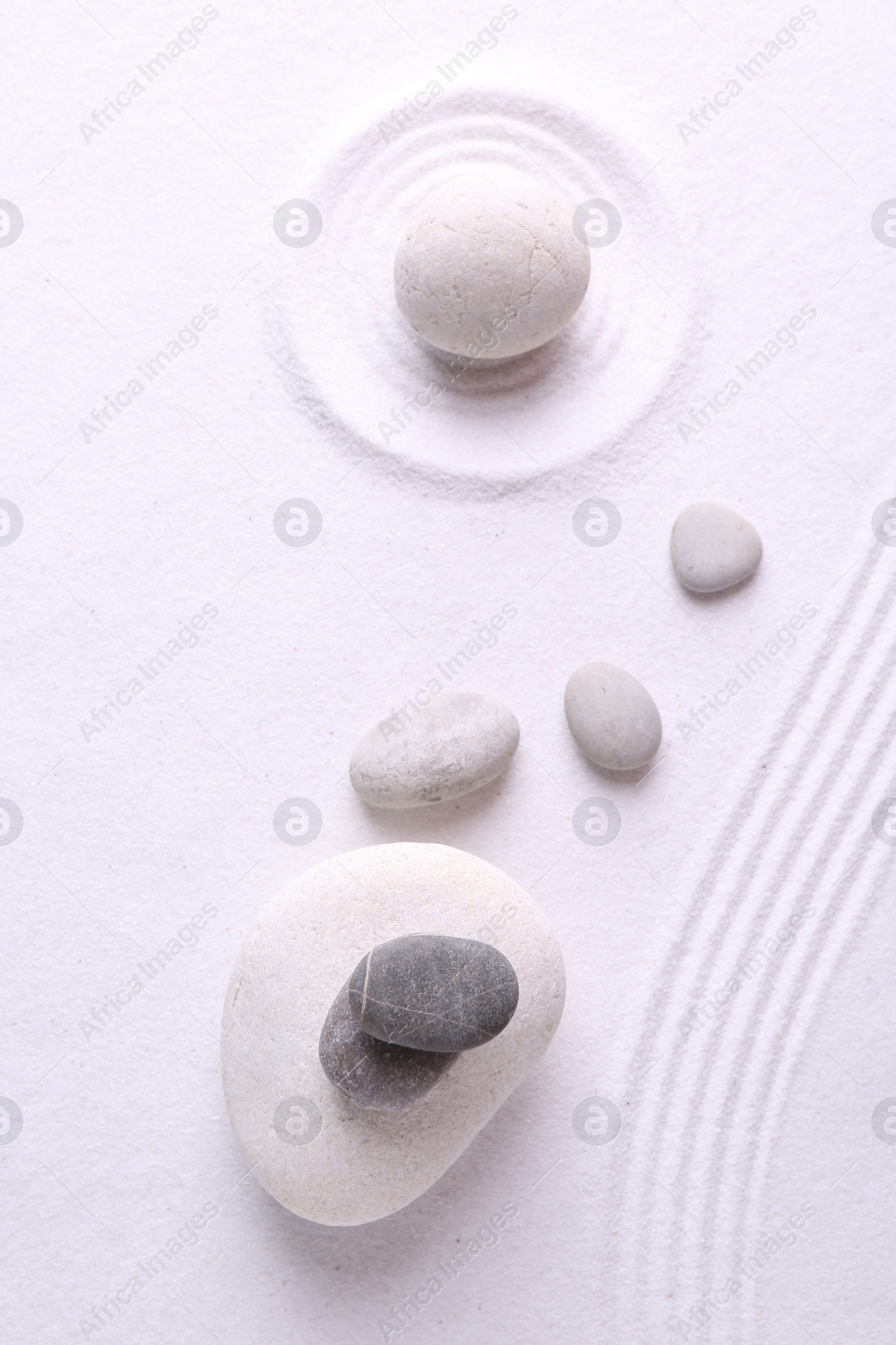 Photo of Zen garden stones on white sand with pattern, flat lay