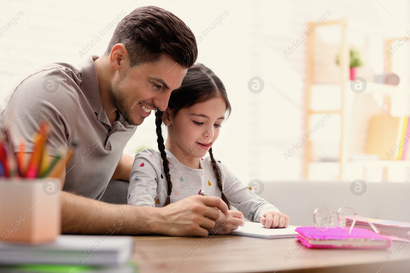 Photo of Man helping his daughter with homework at table indoors