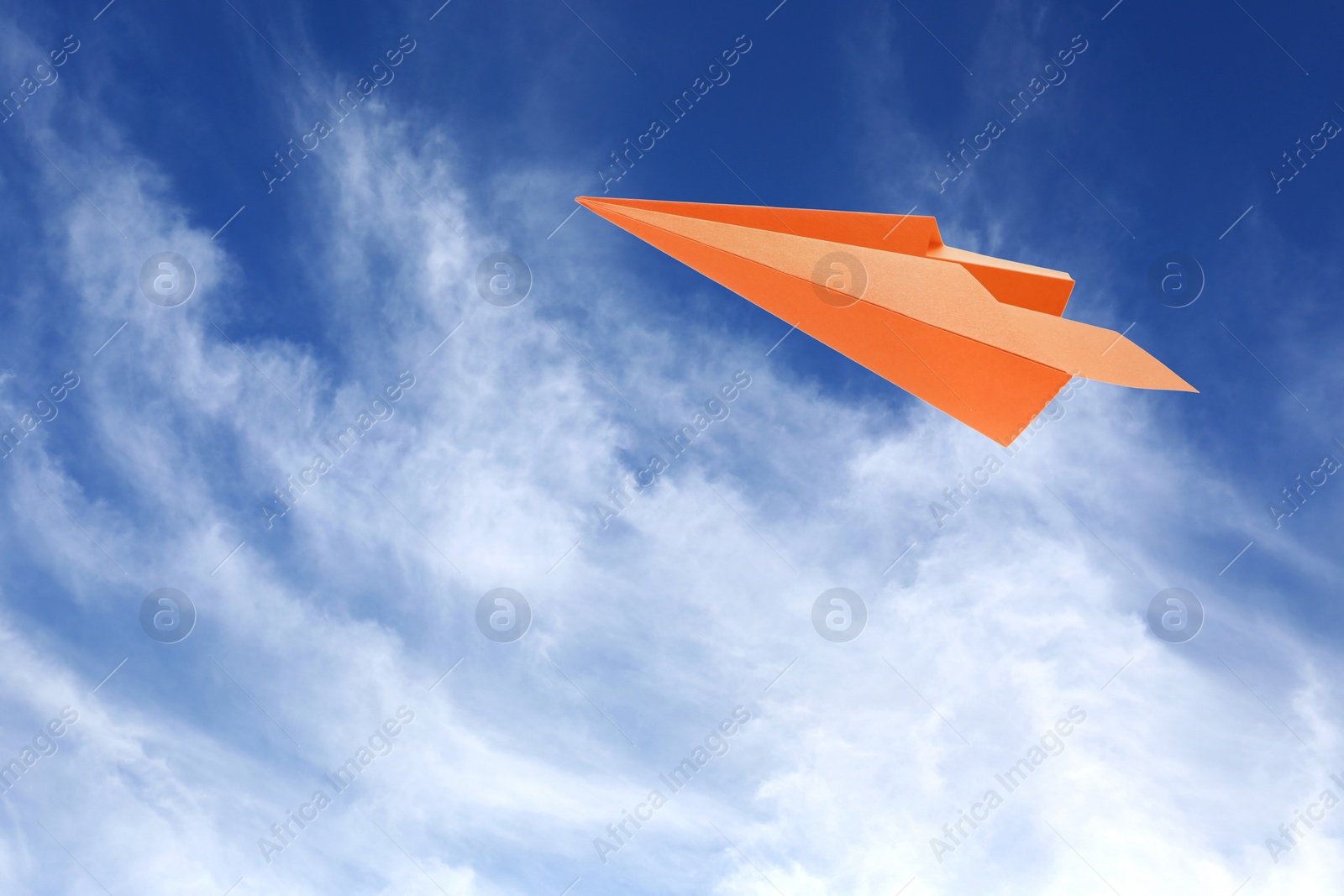 Image of Orange paper plane flying in blue sky with clouds