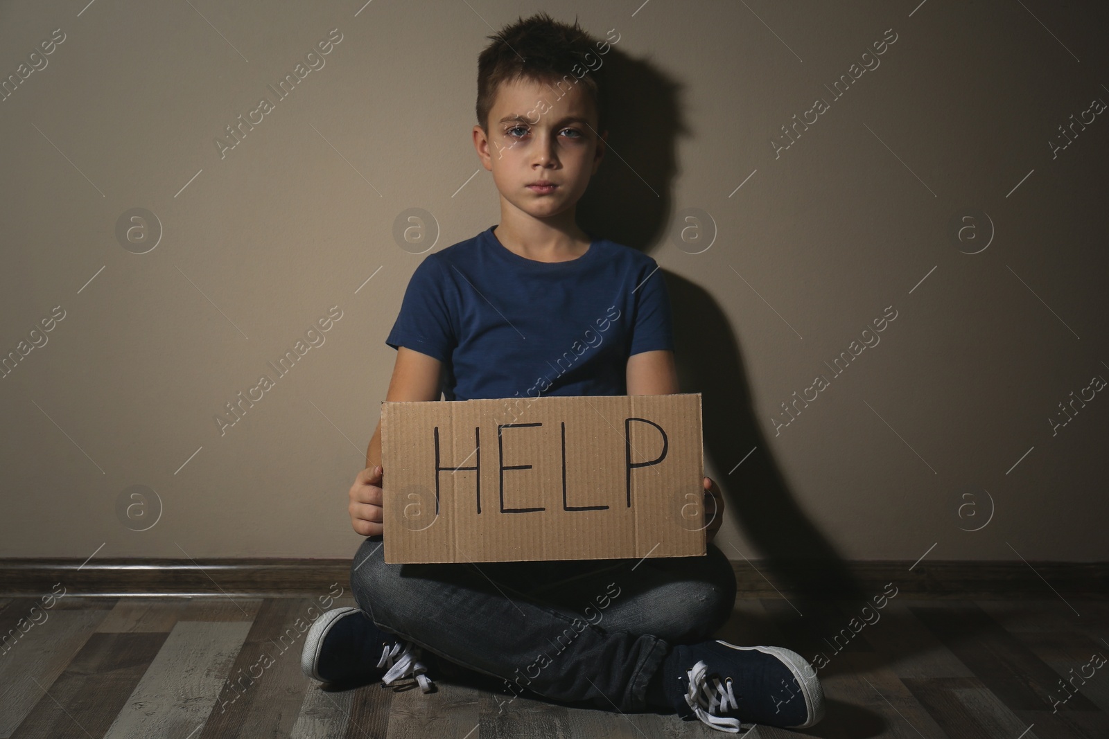 Photo of Abused little boy with sign HELP near beige wall. Domestic violence concept