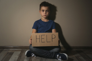 Abused little boy with sign HELP near beige wall. Domestic violence concept