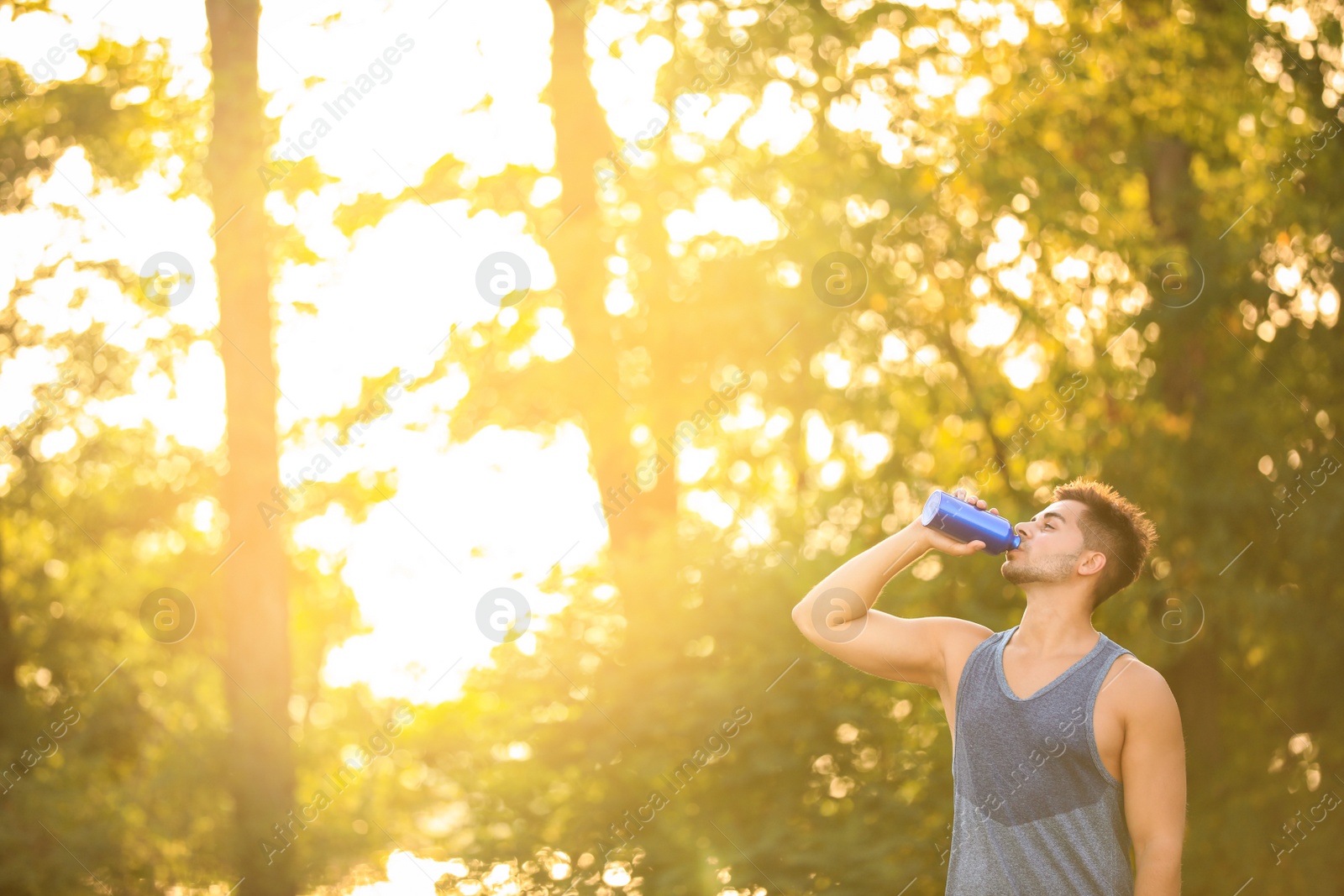 Photo of Young man drinking water from sport bottle after training in park