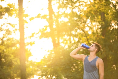 Photo of Young man drinking water from sport bottle after training in park