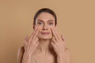 Photo of Woman massaging her face on beige background