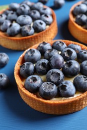 Photo of Tartlets with fresh blueberries on blue table, closeup. Delicious dessert
