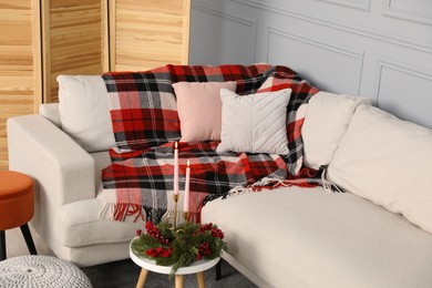 Sofa with pillows, candles and Christmas decoration on table in living room