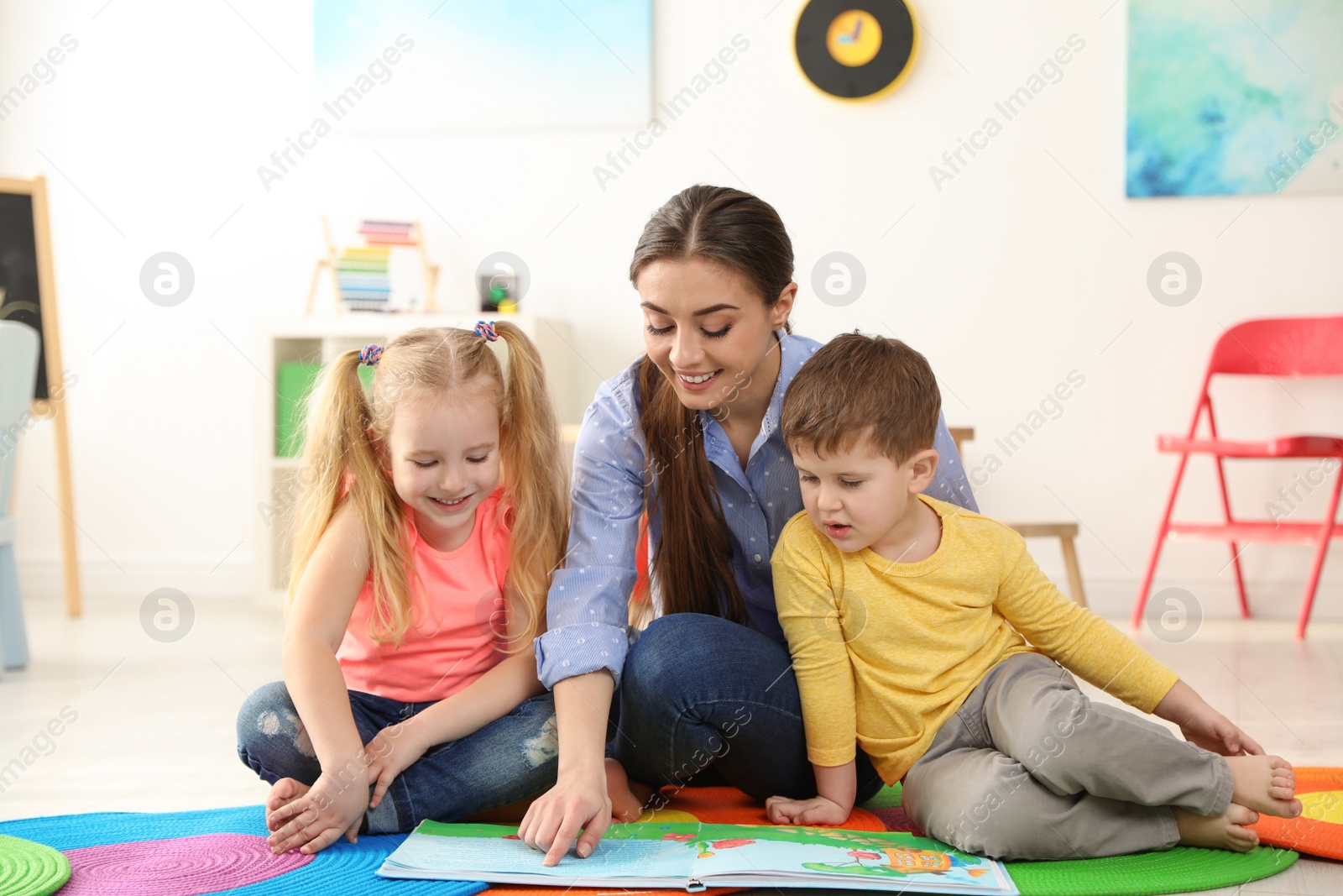 Photo of Kindergarten teacher reading book to children indoors. Learning and playing