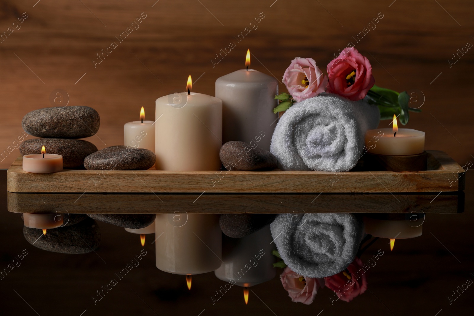 Photo of Beautiful composition with spa stones, flowers and burning candles on mirror table against wooden background