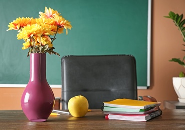 Photo of Bouquet of flowers, apple and notebooks on table in classroom. Teacher day celebration