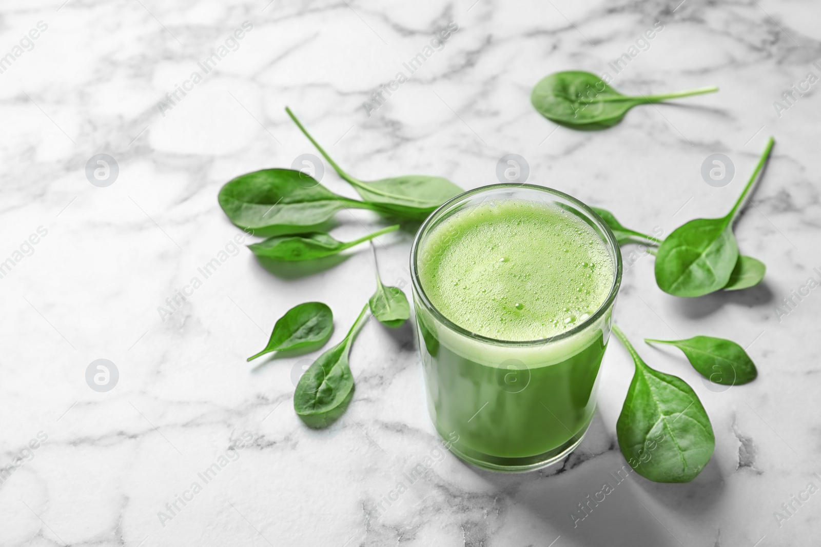 Photo of Glass with delicious detox juice and spinach on marble background