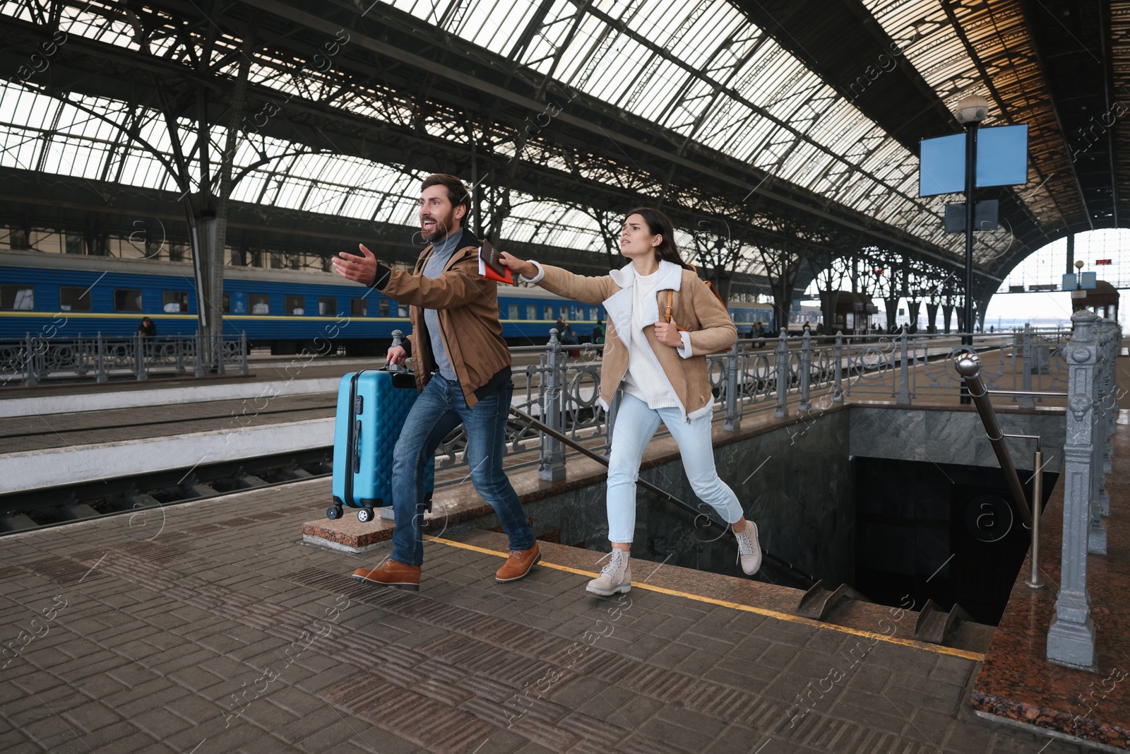 Photo of Being late. Worried couple with suitcase running at train station