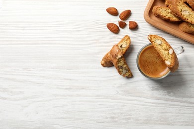 Tasty cantucci, cup of aromatic coffee and nuts on white wooden table, flat lay with space for text. Traditional Italian almond biscuits