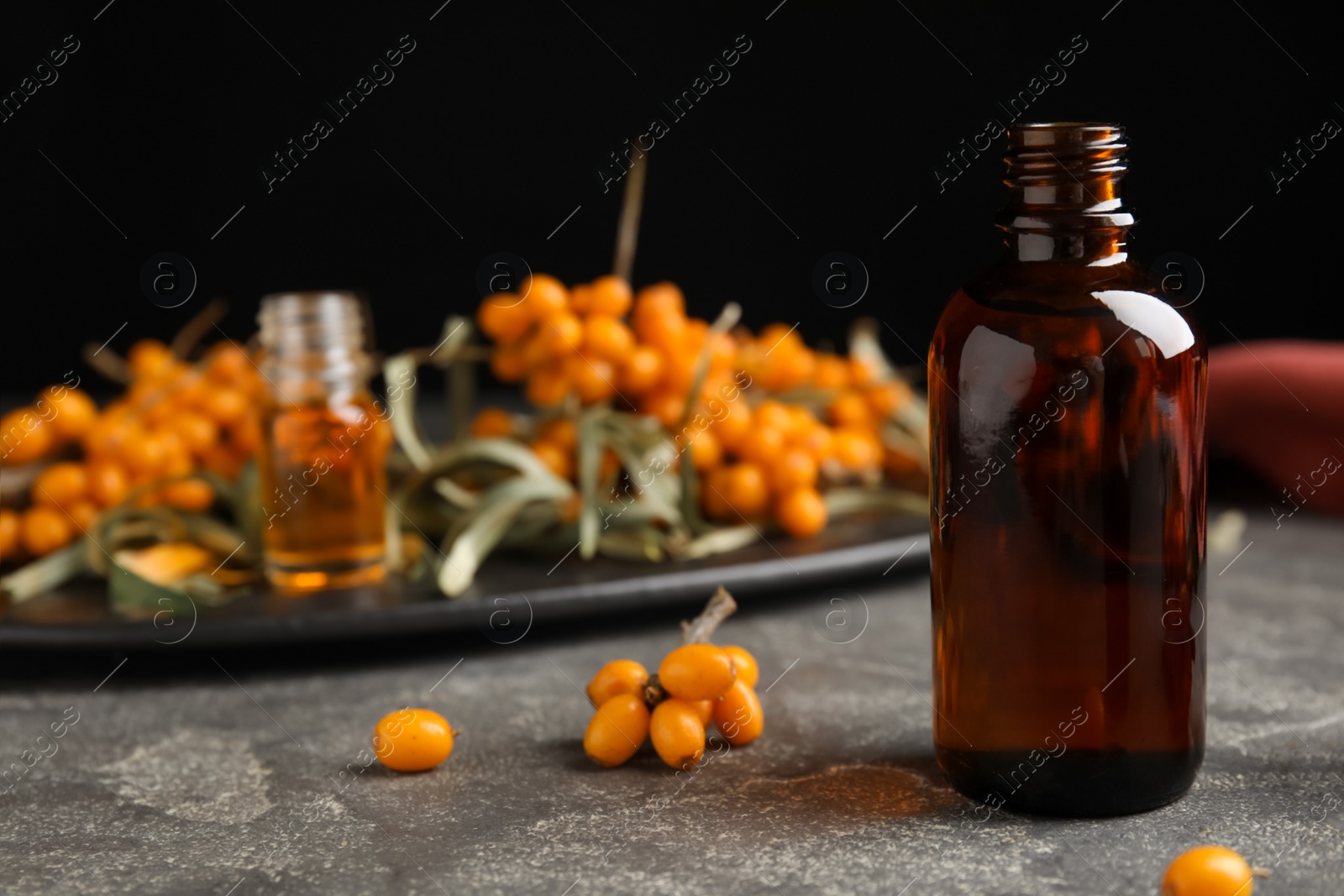 Photo of Ripe sea buckthorn and bottle of essential oil on grey table against black background