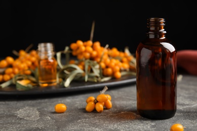 Photo of Ripe sea buckthorn and bottle of essential oil on grey table against black background