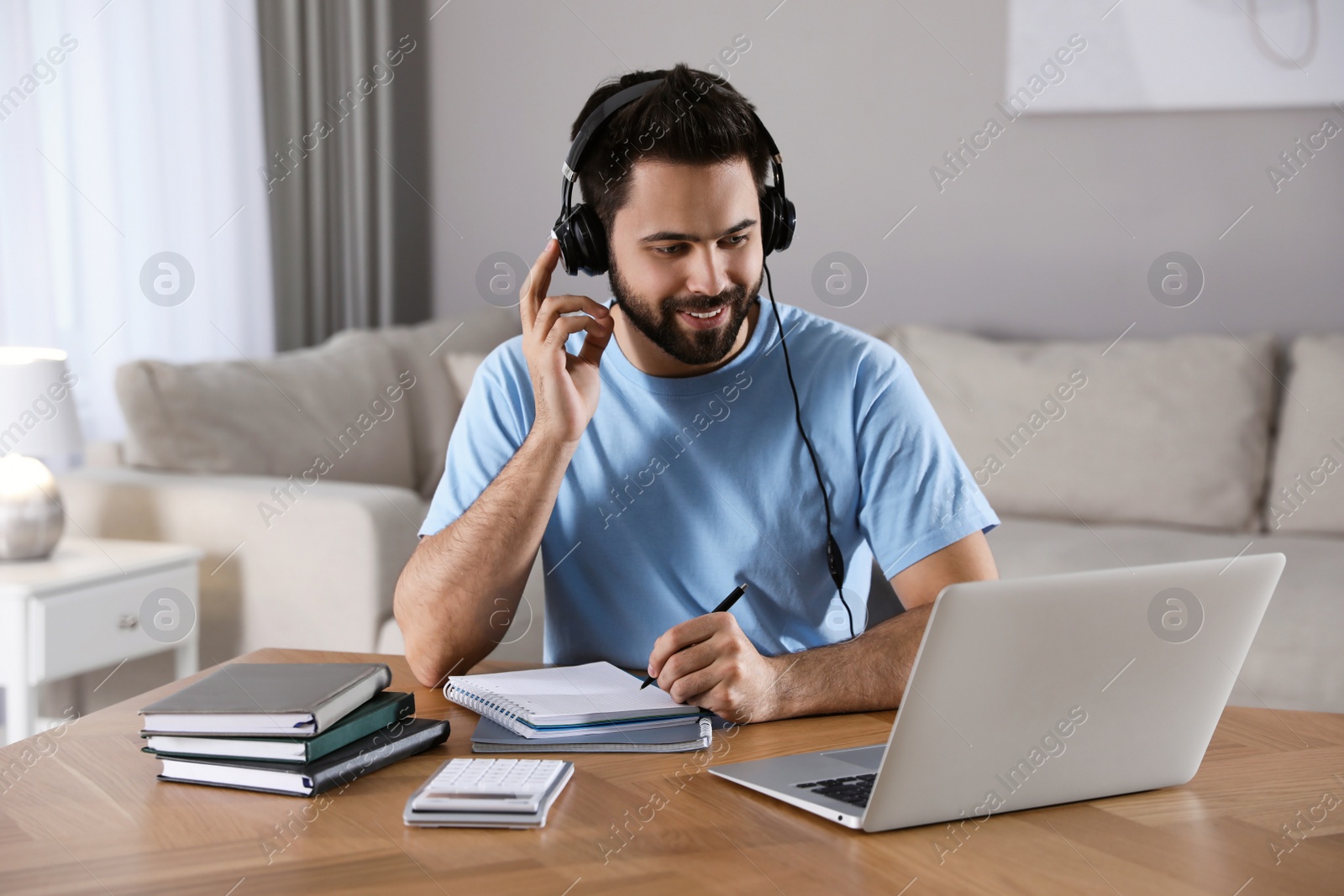 Photo of Young man watching webinar at table in room