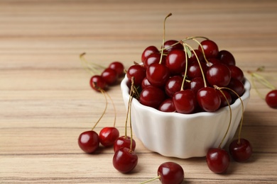 Photo of White bowl of delicious cherries on wooden table, space for text