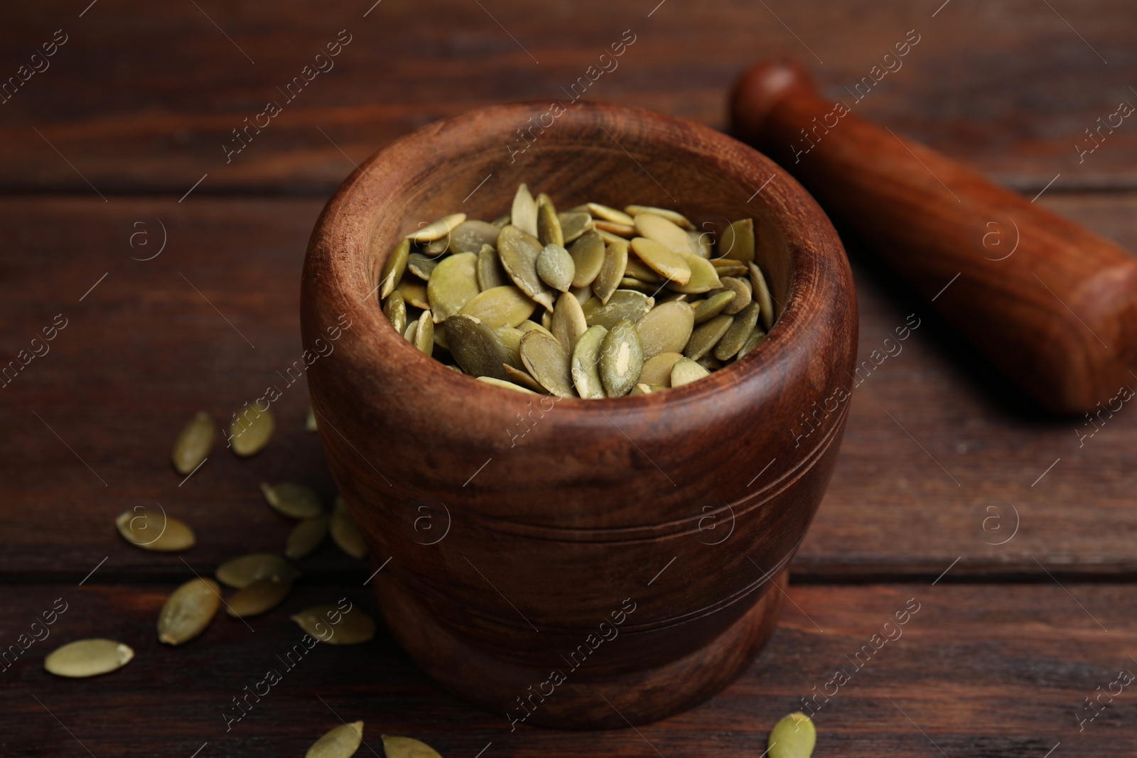 Photo of Mortar with pumpkin seeds and pestle on wooden table, closeup