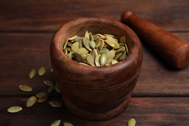 Photo of Mortar with pumpkin seeds and pestle on wooden table, closeup