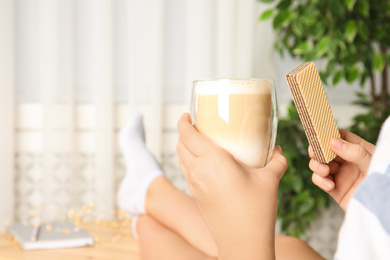 Woman having delicious wafer and coffee for breakfast indoors, closeup