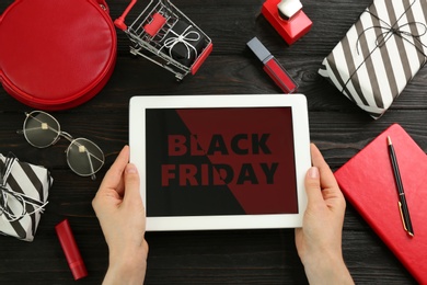 Photo of Woman with tablet surrounded by gifts and accessories at wooden table, top view. Black Friday sale