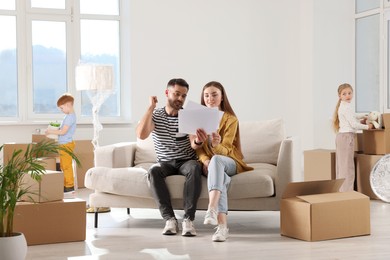 Photo of Family settling into home. Happy wife with husband choosing interior details while children unpacking boxes in new apartment. Moving day