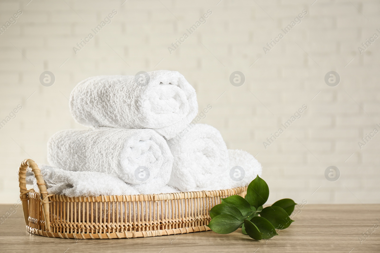 Photo of Wicker basket with rolled bath towels and green branch on wooden table