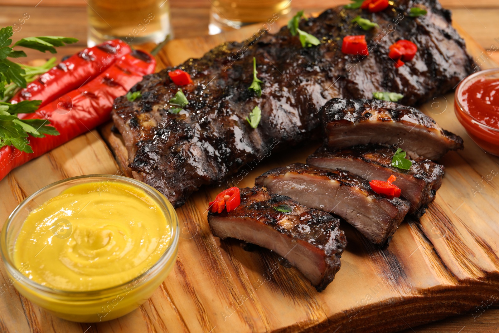 Photo of Tasty grilled ribs and sauce on wooden table, closeup