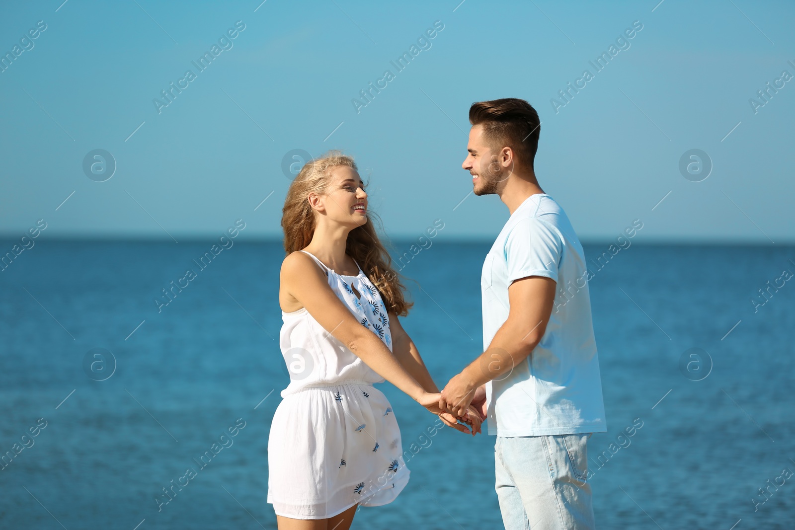 Photo of Happy young couple holding hands at beach on sunny day