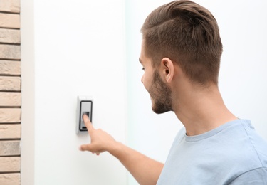 Photo of Young man pressing fingerprint scanner on alarm system indoors