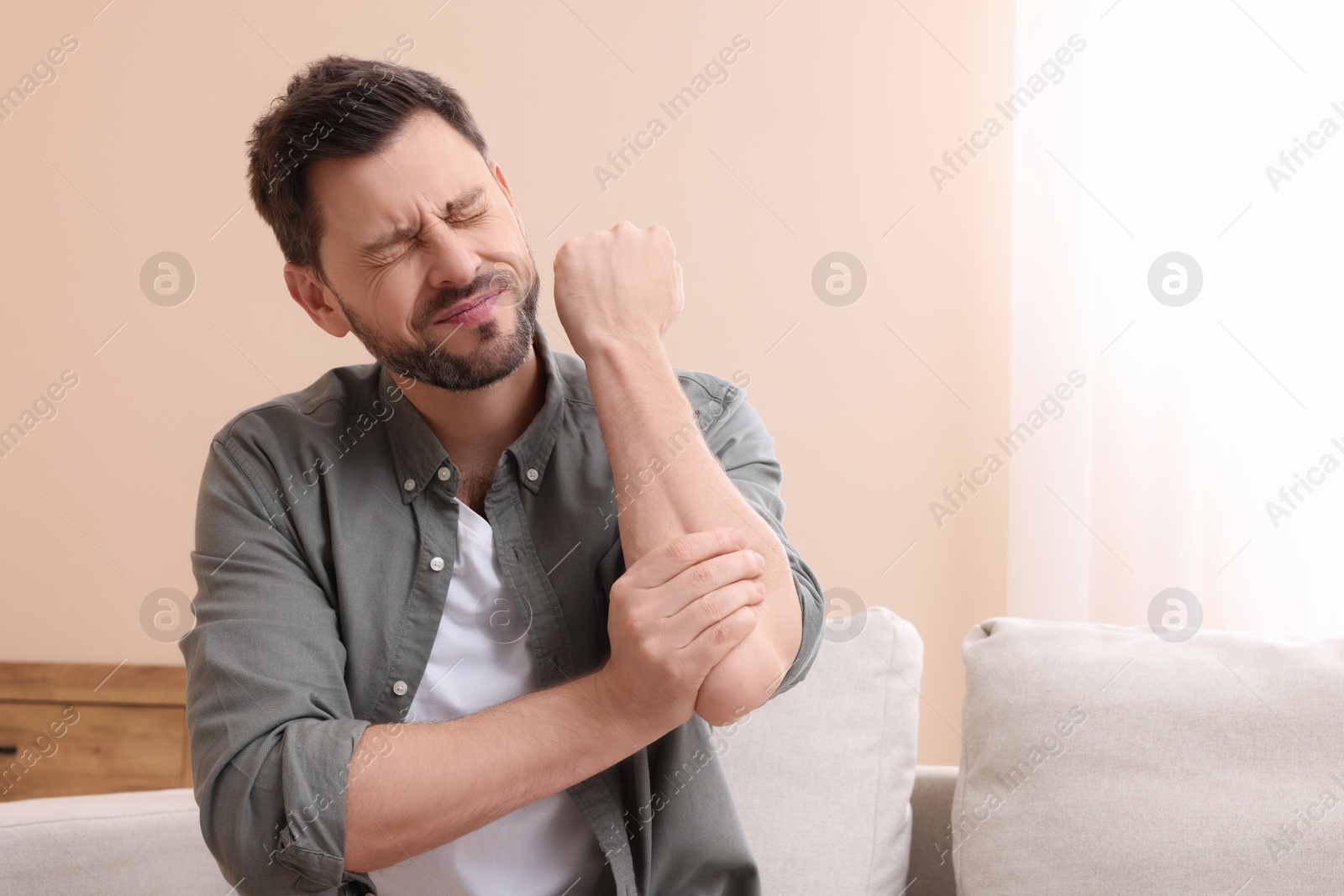 Photo of Man suffering from pain in his elbow at home, space for text. Arthritis symptoms