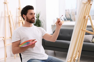 Photo of Man painting in studio. Using easel to hold canvas