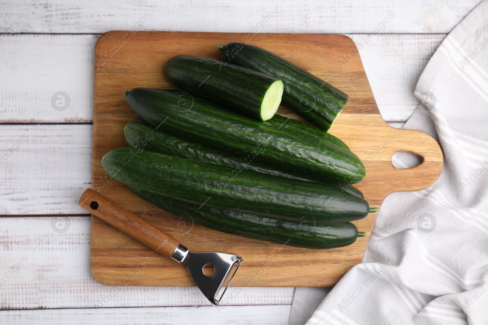 Photo of Fresh cucumbers and peeler on white wooden table, top view