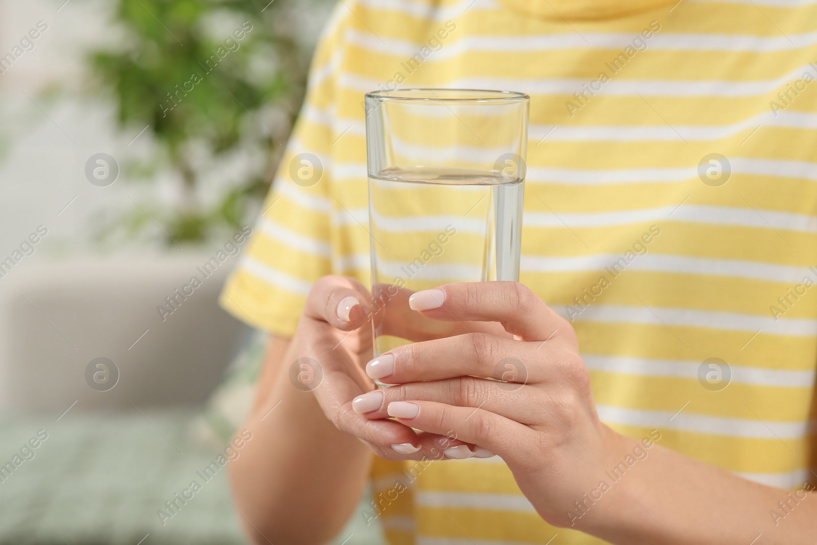 Photo of Healthy habit. Closeup of woman holding glass with fresh water indoors